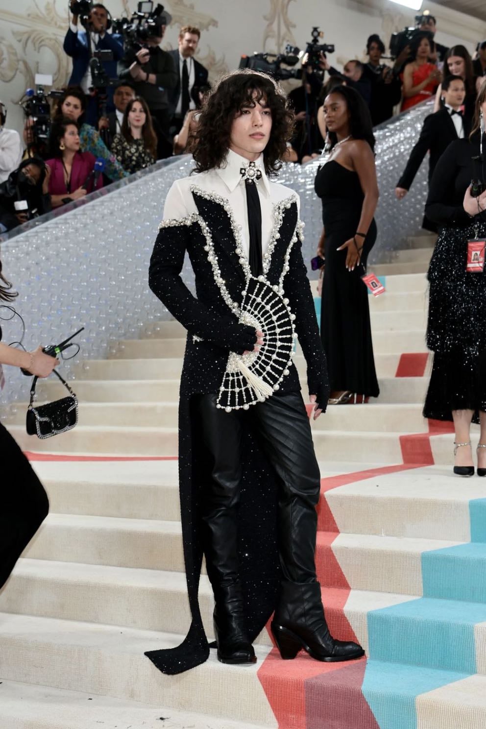 conan gray - custom balmain
designed by olivier rousteing. a white shirting and black tie with an off-the-shoulder black tweed jacket with hand-embroidered pearls, a high v-neck collar and attached gloves, paired with leather diamond quilted high heel pants and a black pearl embellished fan
