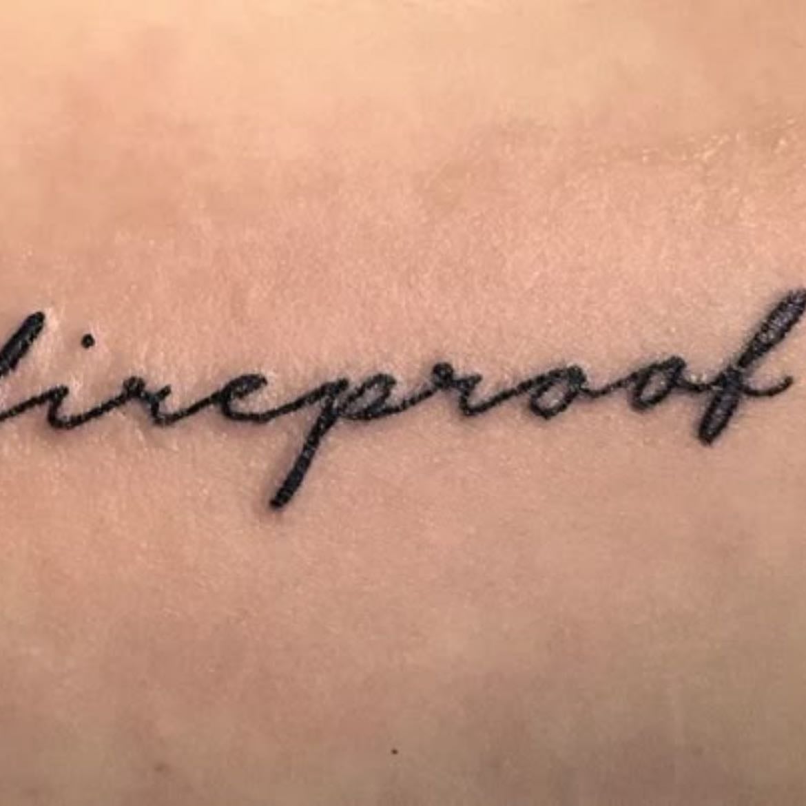 one direction tattoo - maybe ‘fireproof’ or ‘through the dark’ just below the elbow on the front.