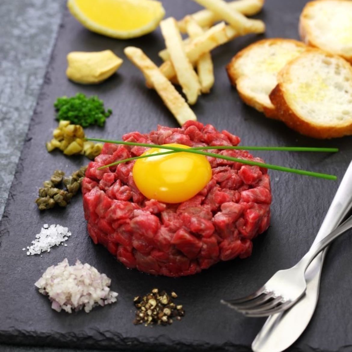 Steak Tartar - Carne de res cruda finamente picada, sazonada con sal, pimienta, cebolla, alcaparras y otros condimentos como salsa Worcesthire, mostaza y yema de huevo cruda.